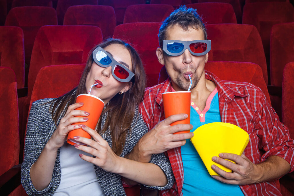 spectators sitting in the cinema and watching movie with cups of cola and popcorn