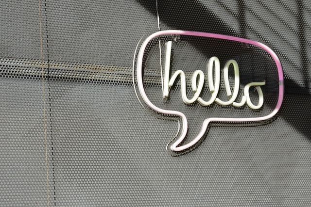 neon sign on plain wall displaying the word hello inside a speech bubble