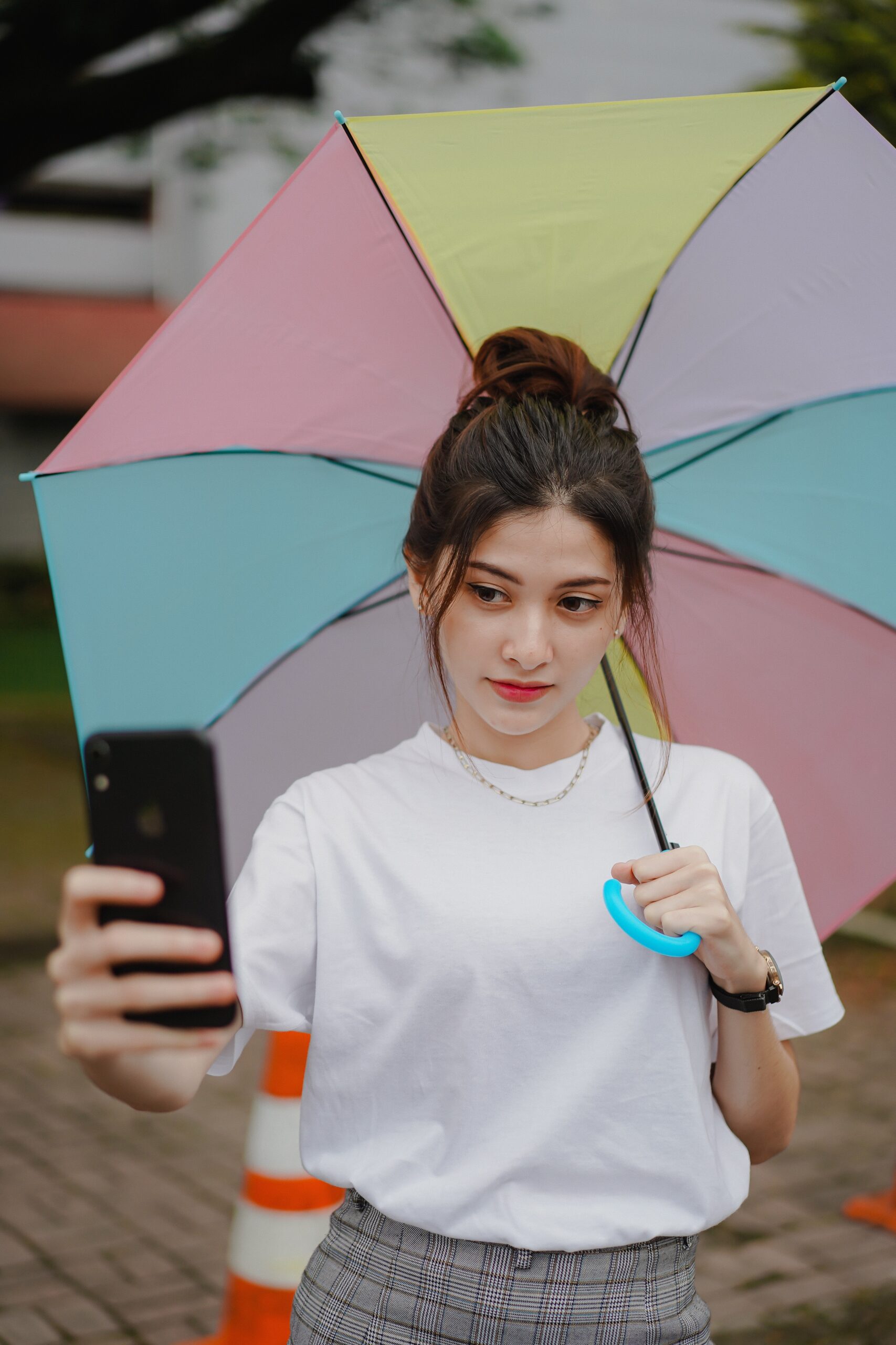 A girl with an umbrella takes a selfie with a phone.