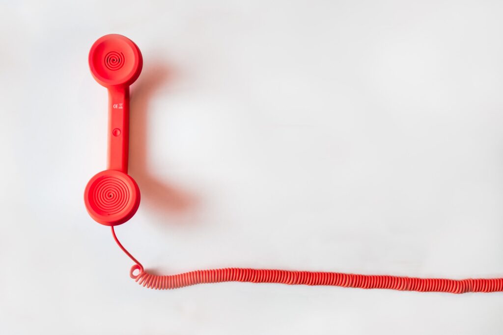 a red telephone with a cord appears flat lay style on a white backdrop