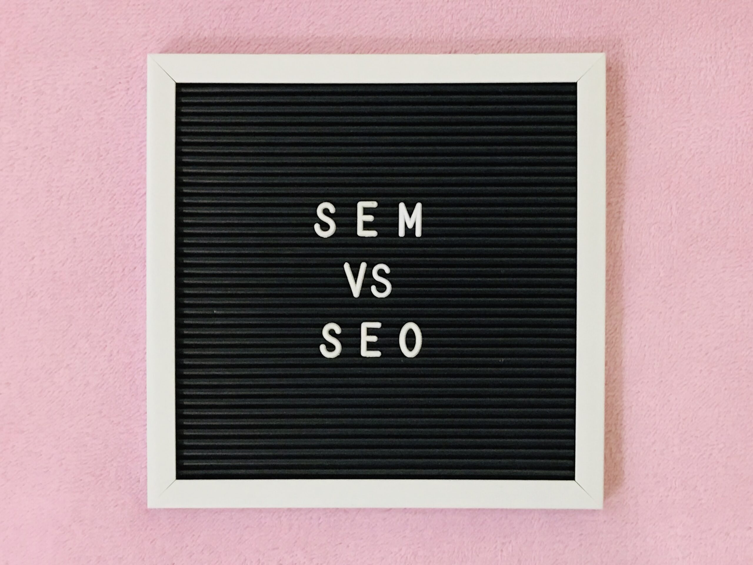 A blackboard has the words "SEM VS SEO" spelled out in white lettering