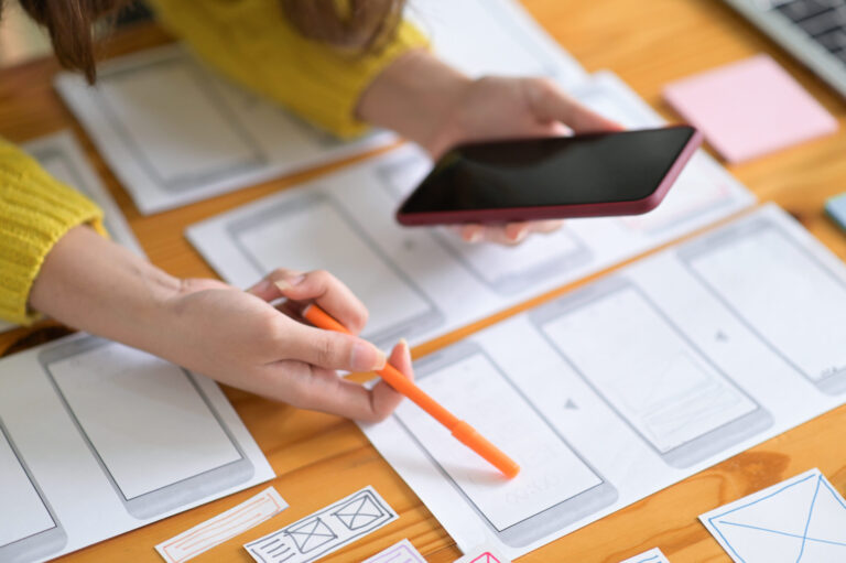 Web designers hold a smartphone as they draw out what the mobile website will look like